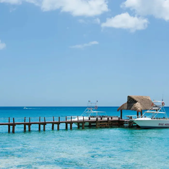 Dive boats docked at a thatched-roof pier on clear blue sea, ideal for scuba excursions.
