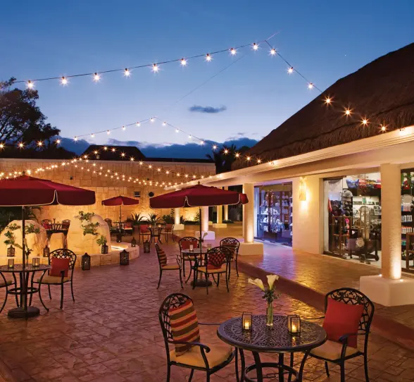 Evening lights strung above a charming open-air plaza with patio seating and boutique-style shops.