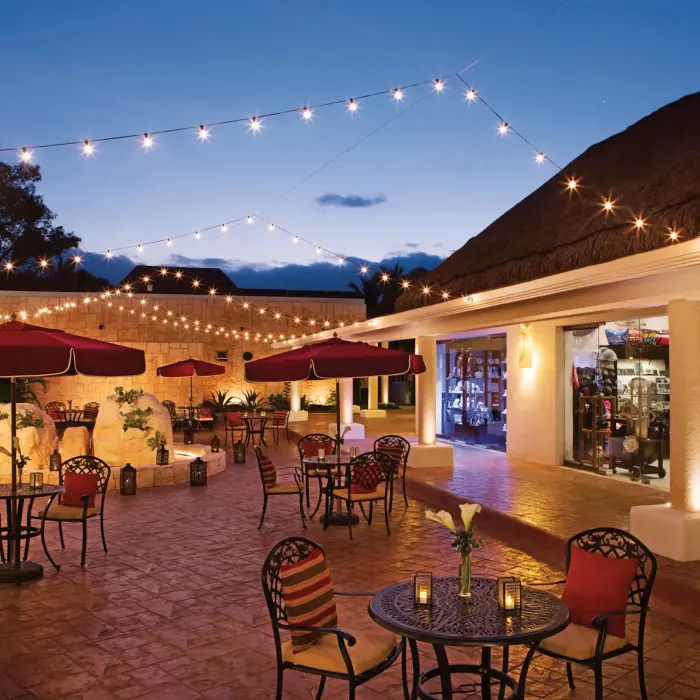 Evening lights strung above a charming open-air plaza with patio seating and boutique-style shops.