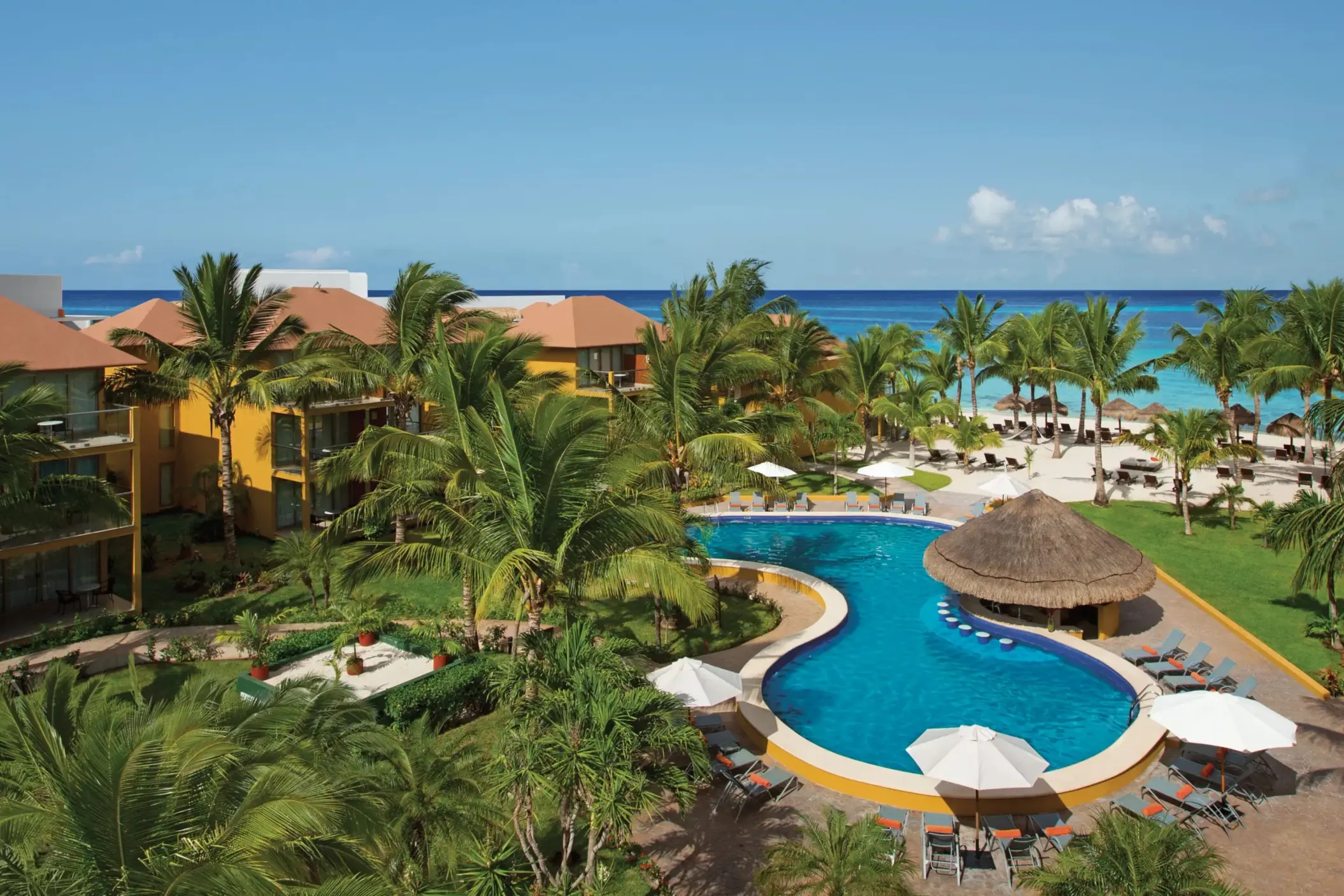 Lagoon-style pool with swim-up bar surrounded by palm trees and tropical gardens near the beach.