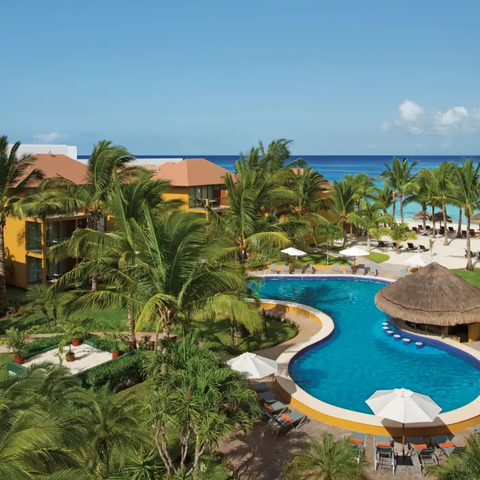 Lagoon-style pool with swim-up bar surrounded by palm trees and tropical gardens near the beach.