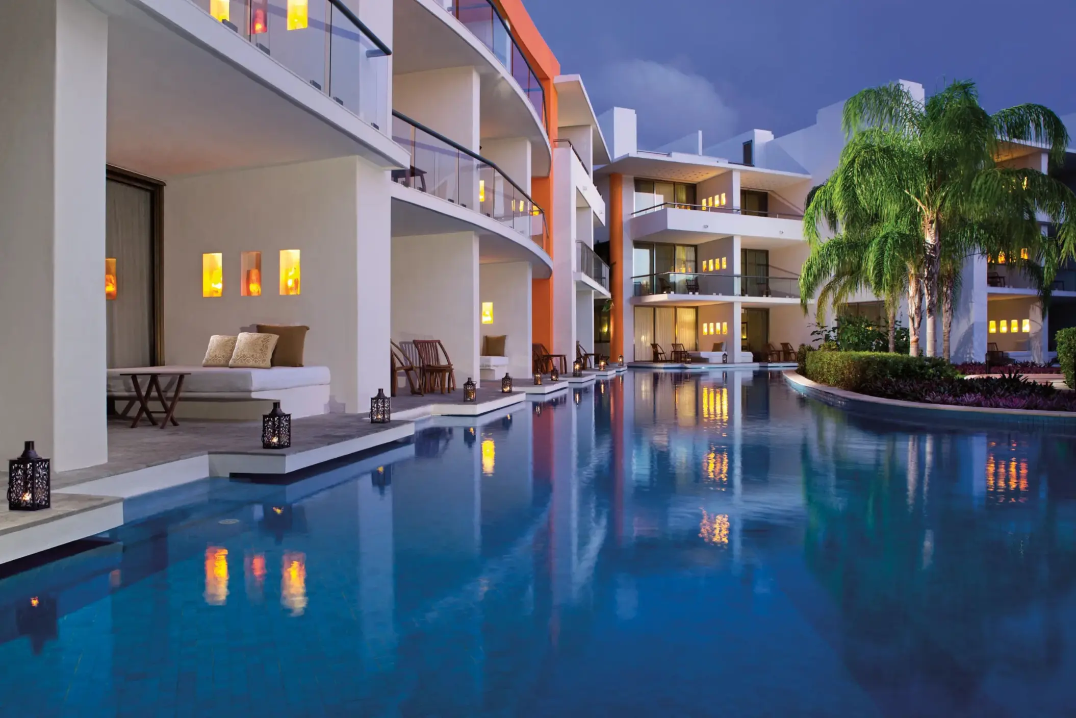 Swim-up suites lit warmly at night with lanterns reflecting in the calm pool under a twilight sky.