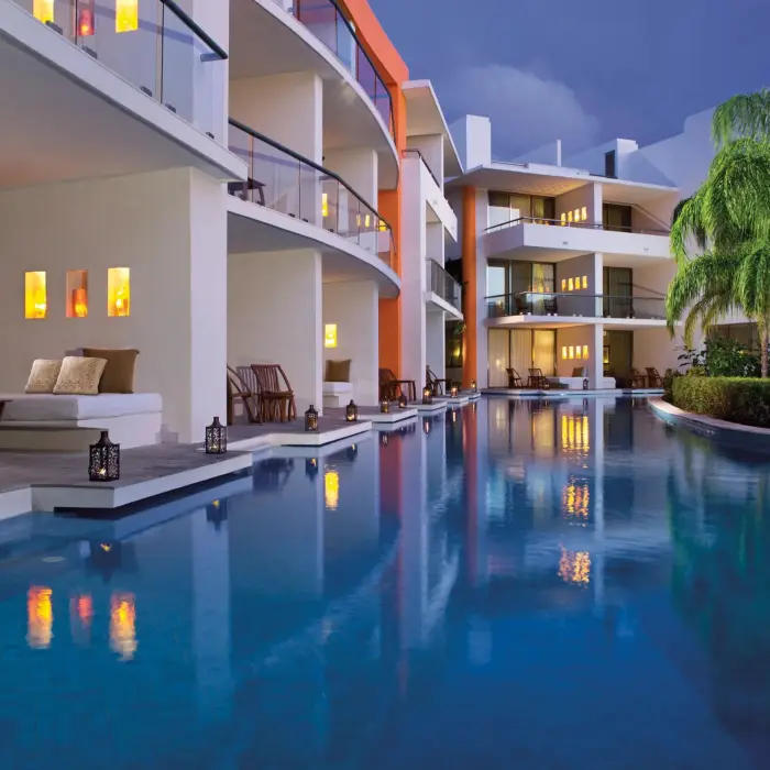 Swim-up suites lit warmly at night with lanterns reflecting in the calm pool under a twilight sky.