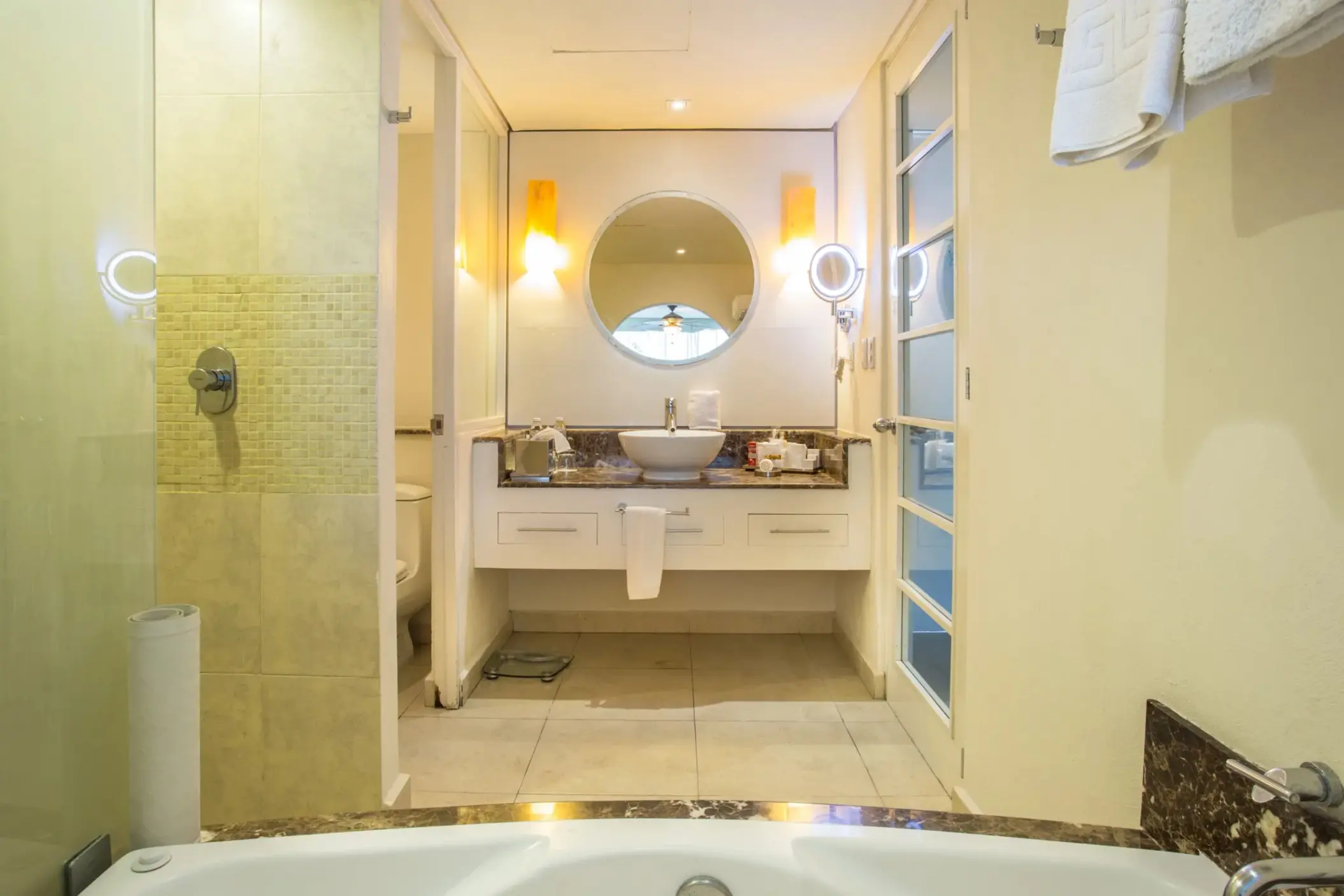 Marble-accented bathroom with soaking tub, walk-in shower, round mirror, and double-sink vanity area.