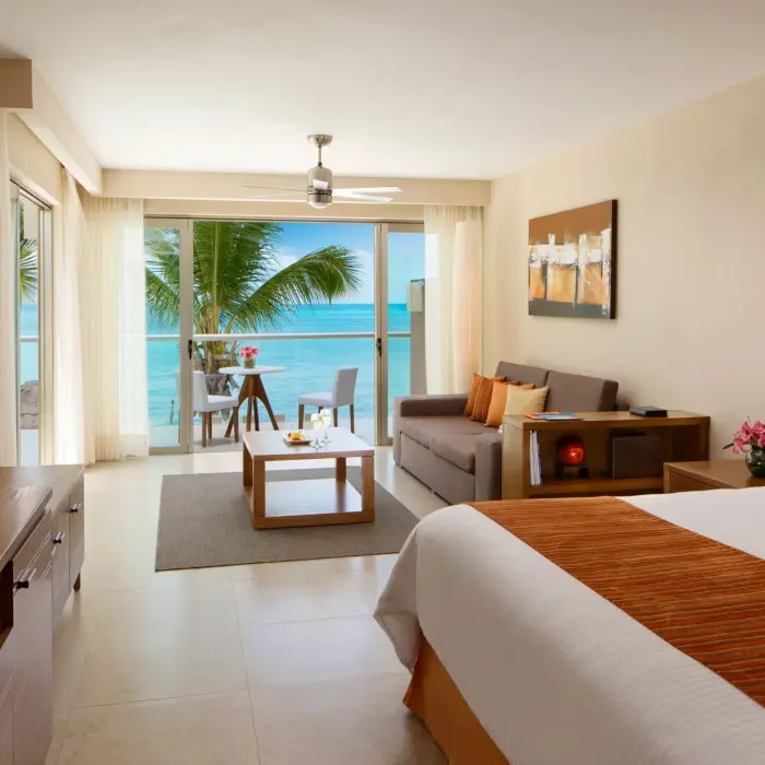Oceanfront junior suite with king bed, bright decor, and private balcony overlooking the sea.