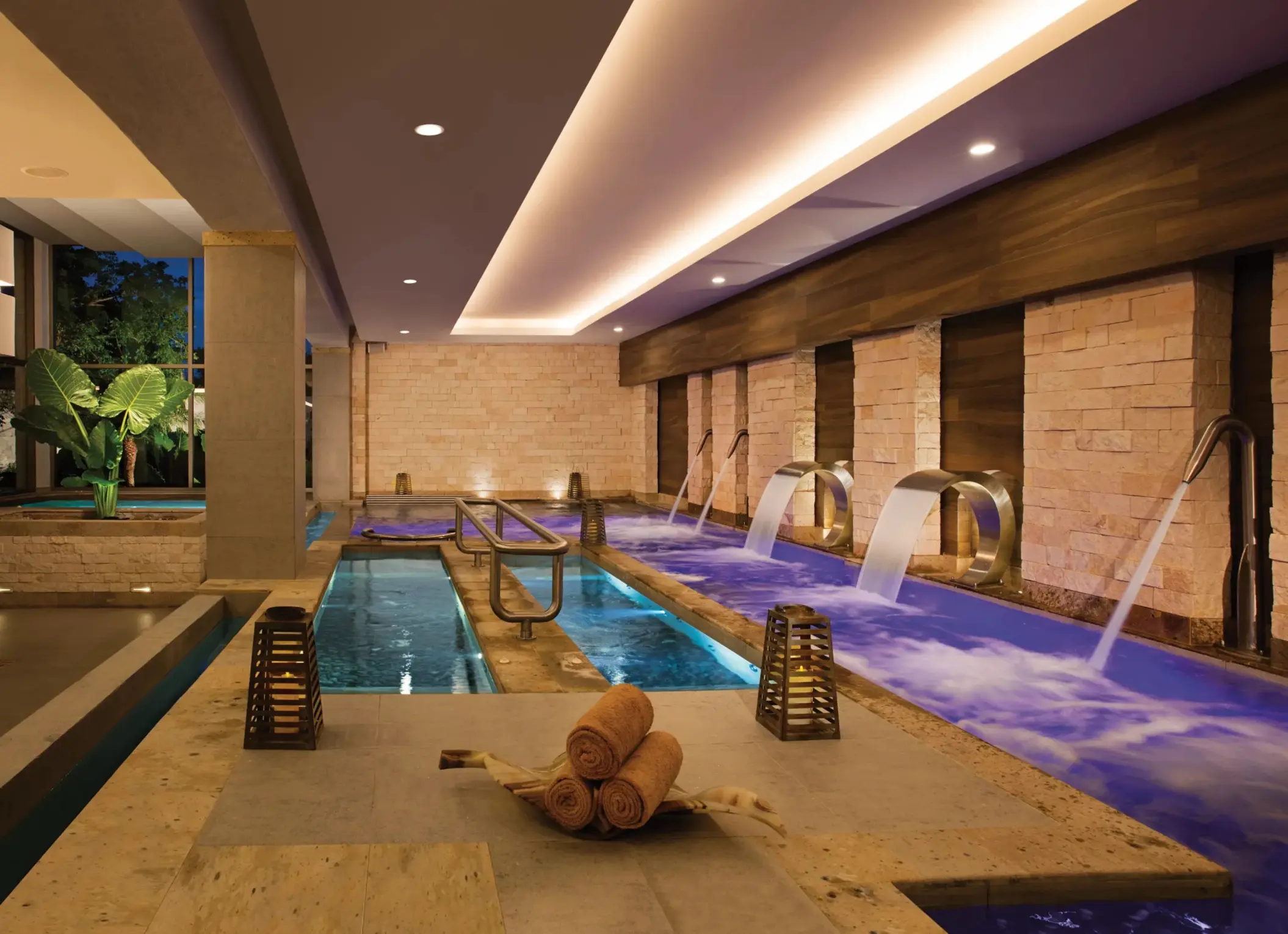 Indoor hydrotherapy circuit with jet pools, water cascades, and relaxing ambiance under soft lighting.