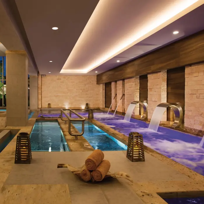 Indoor hydrotherapy circuit with jet pools, water cascades, and relaxing ambiance under soft lighting.