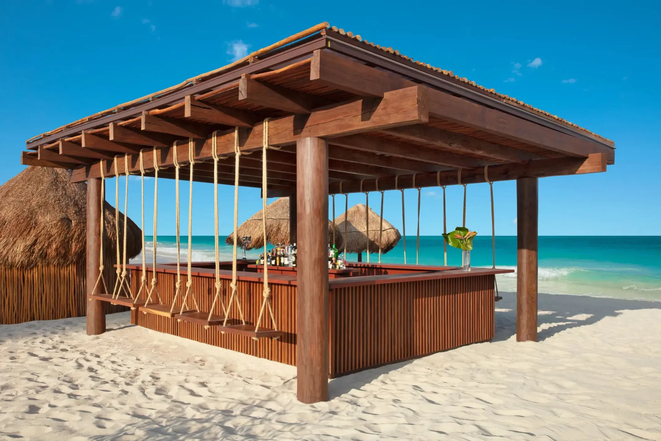 Beachfront swing bar with wood roof and tropical views, serving cocktails just steps from the sand.