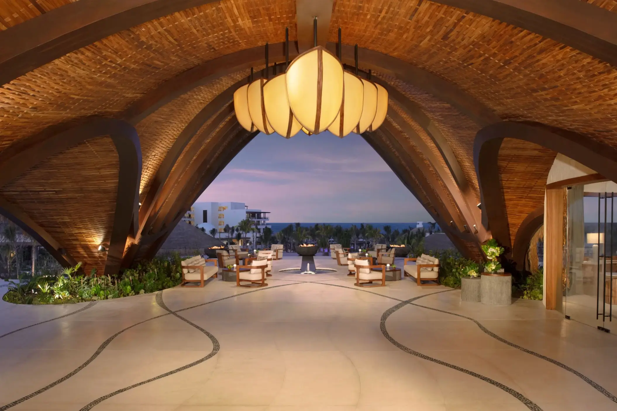 Striking resort lobby with sculptural wood ceiling and open-air views leading out to the ocean.