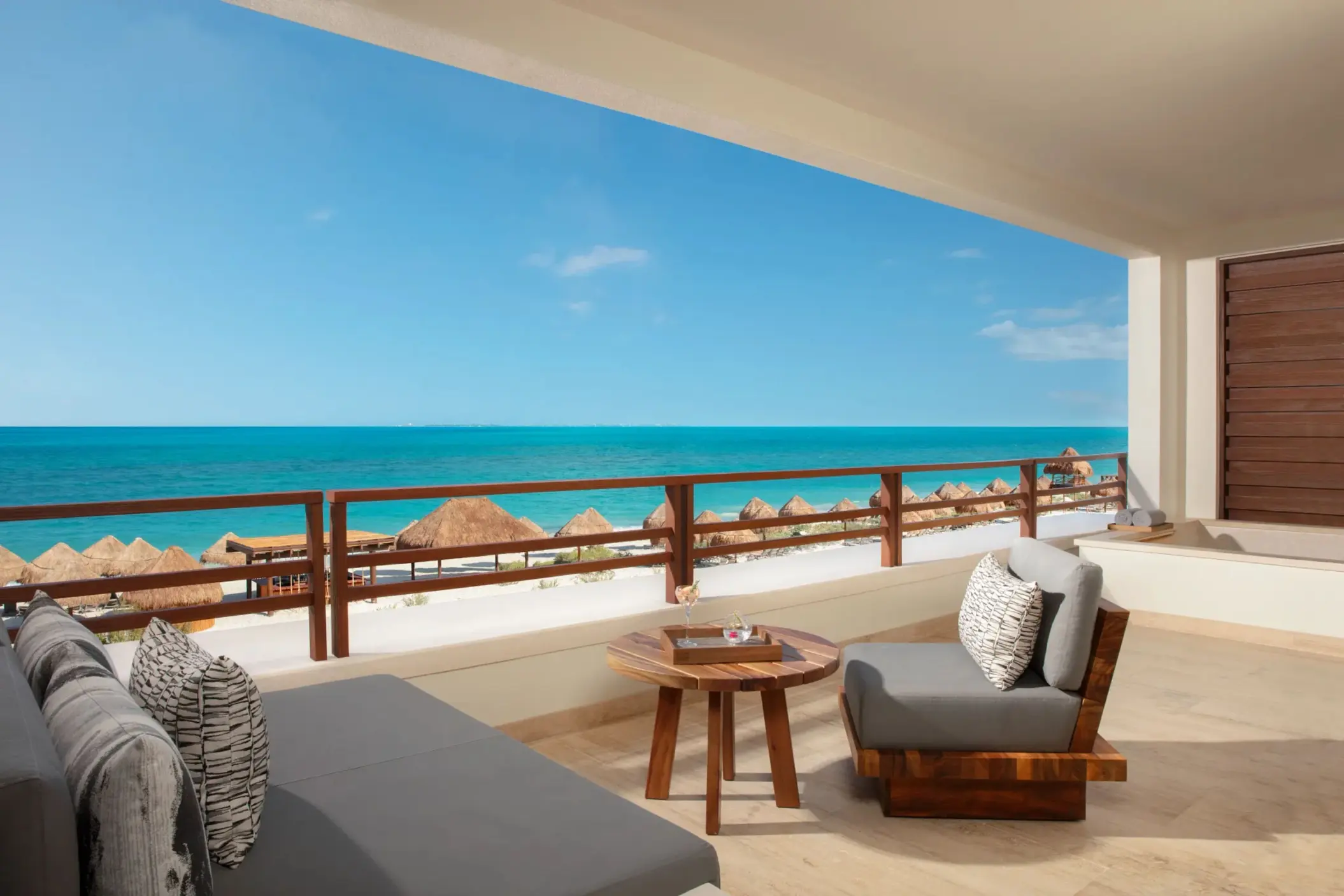 Expansive terrace with full ocean view, lounge beds, dining set, and wooden railing design.