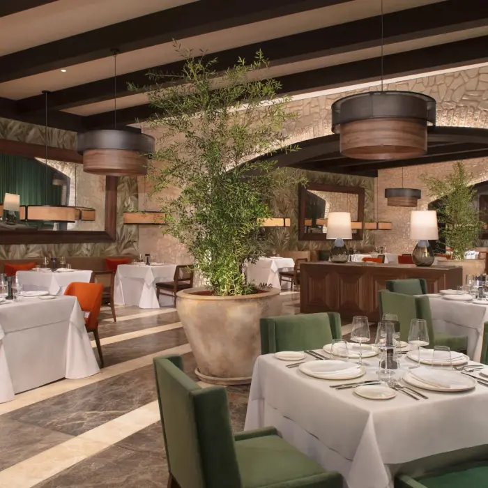 Elegant Italian restaurant interior with stone walls, greenery, and cozy seating under warm lighting.