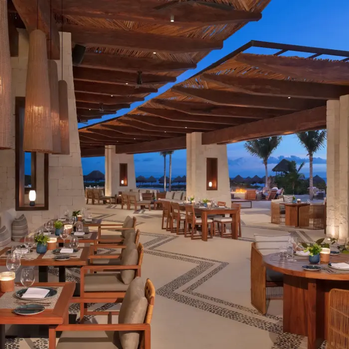 Open-air dining area at Seaside Grill with elegant wood decor, cushioned seating, and ocean views at twilight.