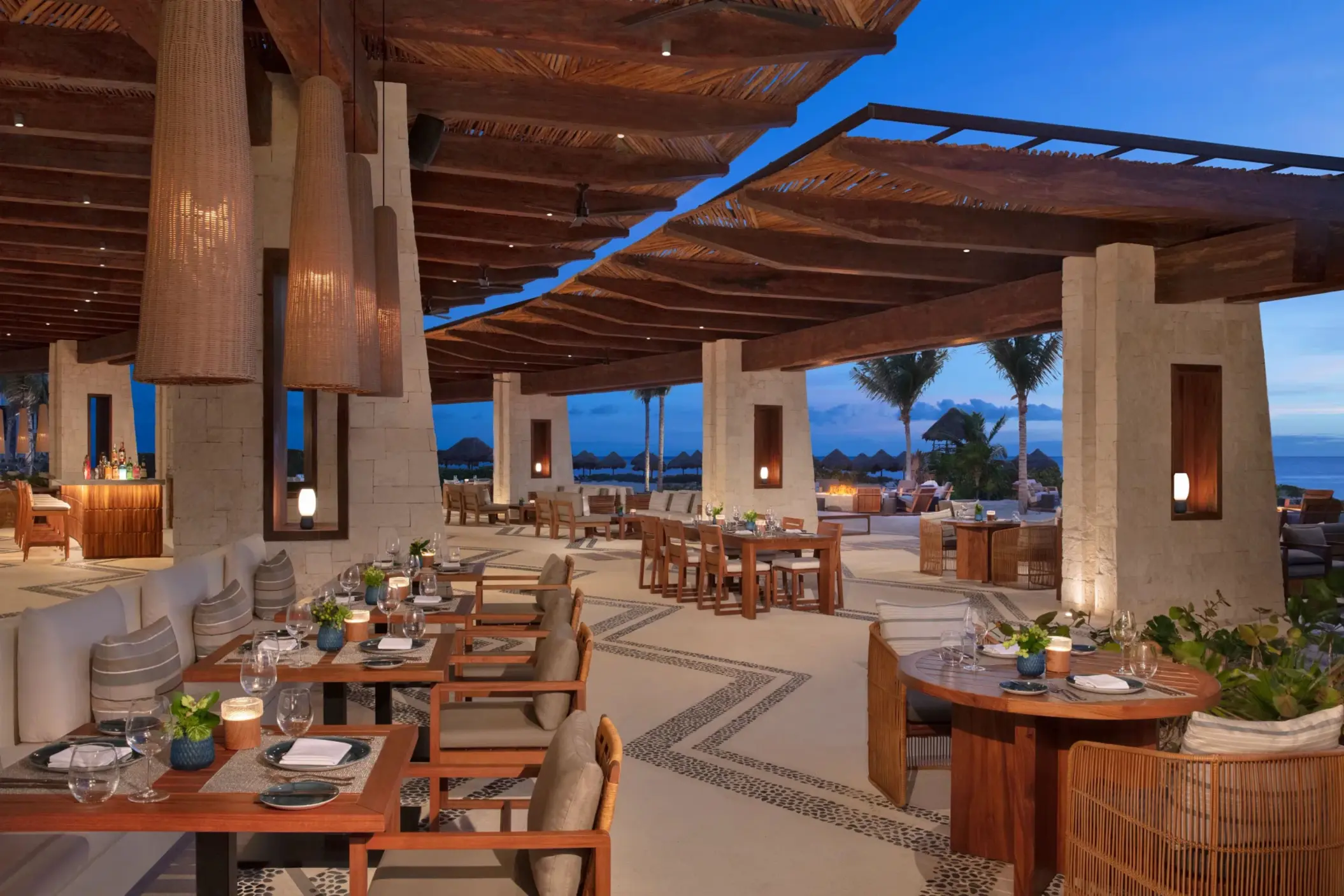 Open-air dining area at Seaside Grill with elegant wood decor, cushioned seating, and ocean views at twilight.