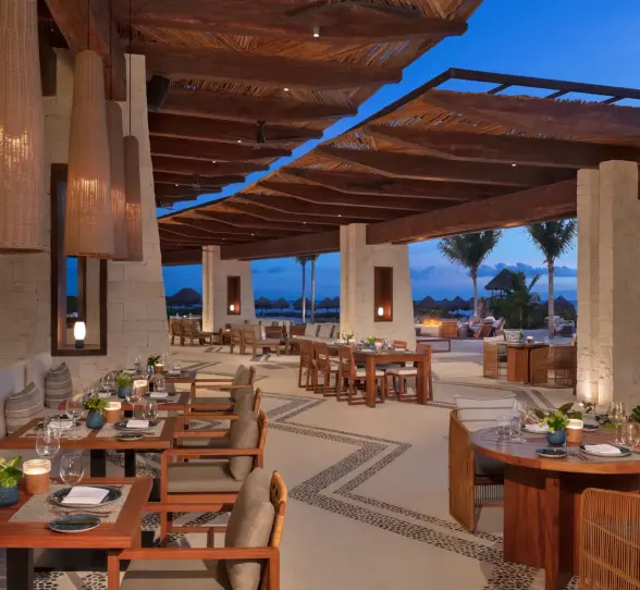 Open-air dining area at Seaside Grill with elegant wood decor, cushioned seating, and ocean views at twilight.