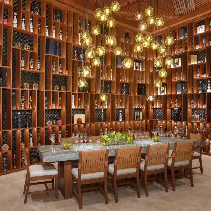 Tequila and mezcal cellar with bottle-lined wooden shelves, glowing pendant lights, and a long tasting table.