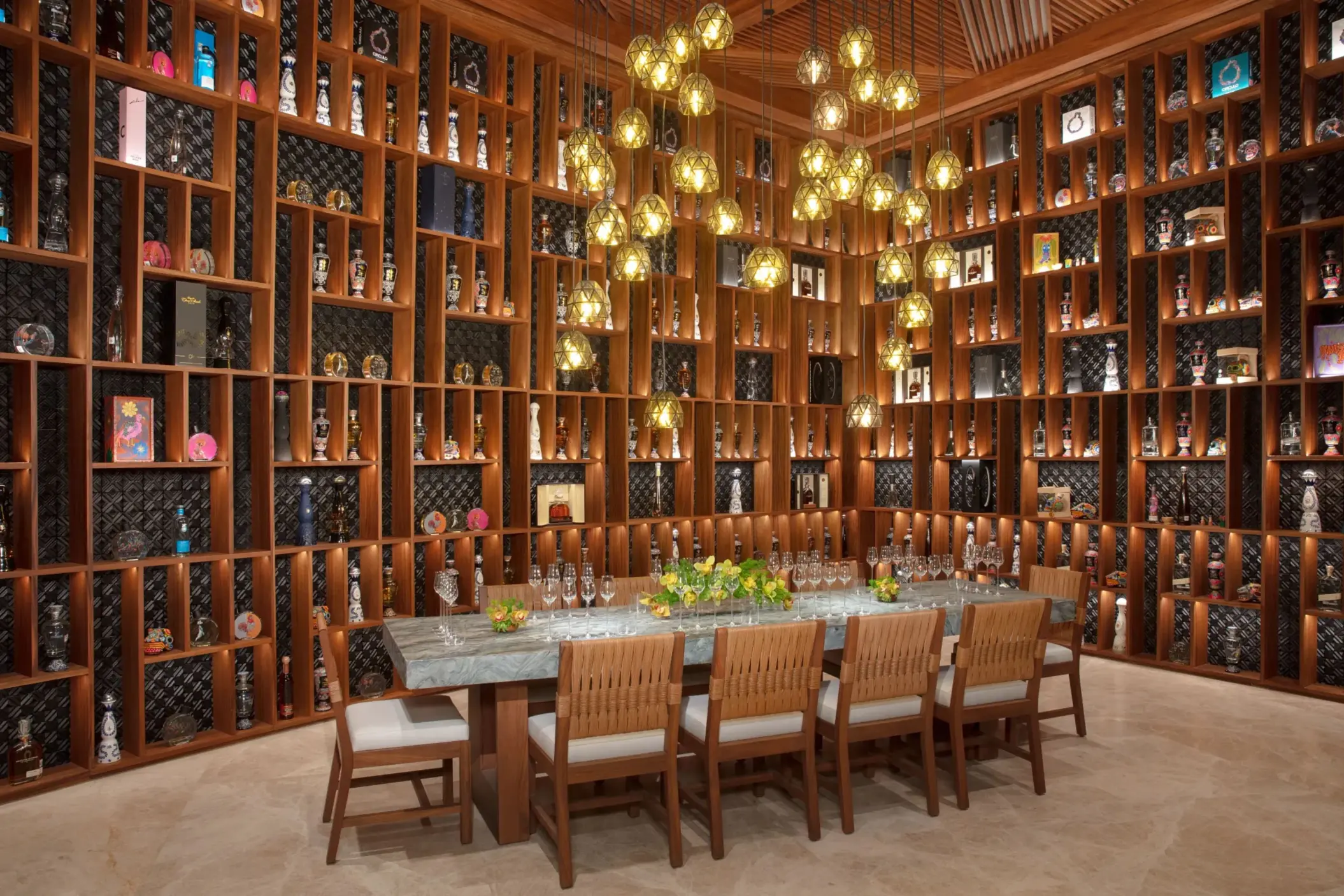 Tequila and mezcal cellar with bottle-lined wooden shelves, glowing pendant lights, and a long tasting table.