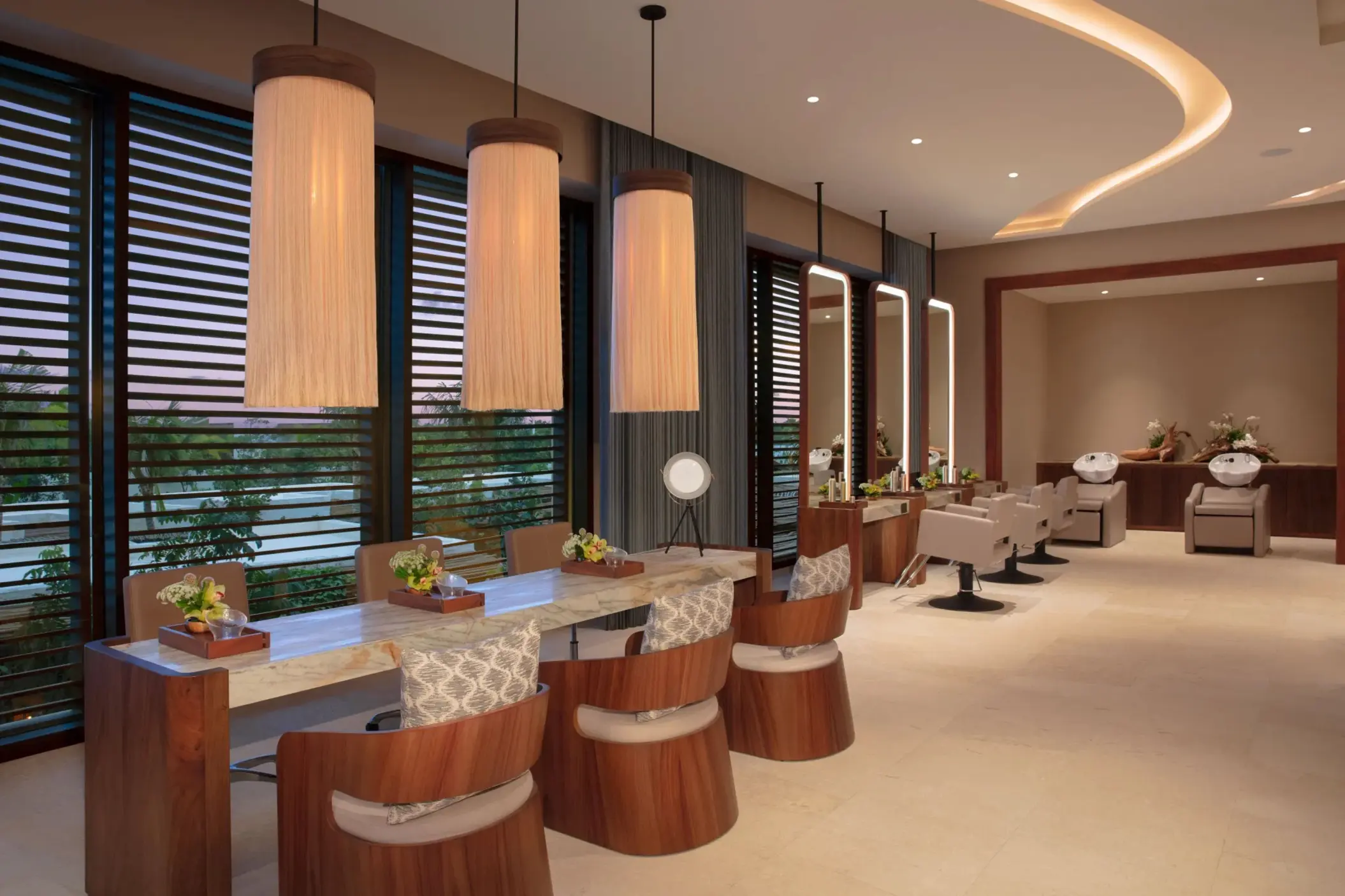 Modern spa salon with styling stations, soft lighting, and plush chairs overlooking tropical scenery.