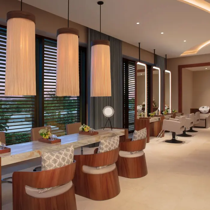 Modern spa salon with styling stations, soft lighting, and plush chairs overlooking tropical scenery.