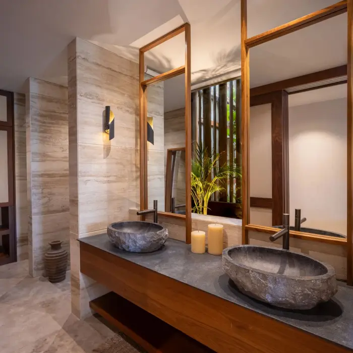 Elegant bathroom with stone vessel sinks, warm lighting, natural textures, and wood-framed mirrors.