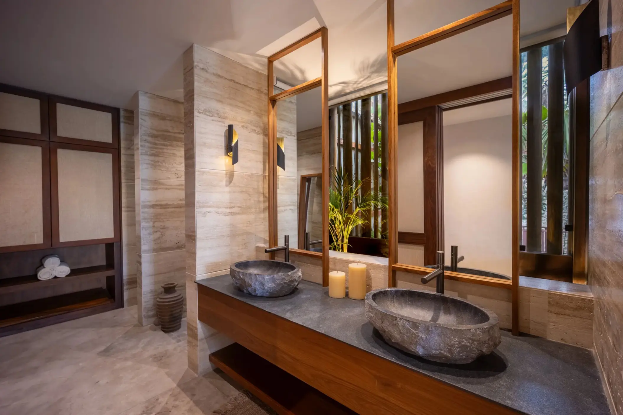 Elegant bathroom with stone vessel sinks, warm lighting, natural textures, and wood-framed mirrors.