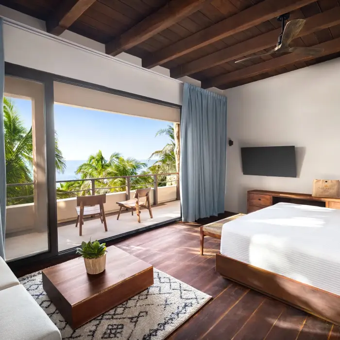 Cozy ocean-view bedroom with wood floors, beamed ceiling, modern decor, and open-air terrace.