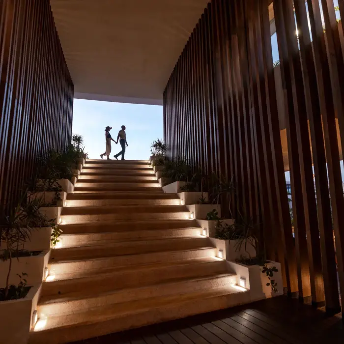 Silhouetted couple walking up illuminated stairs framed by modern wood paneling and soft lighting.