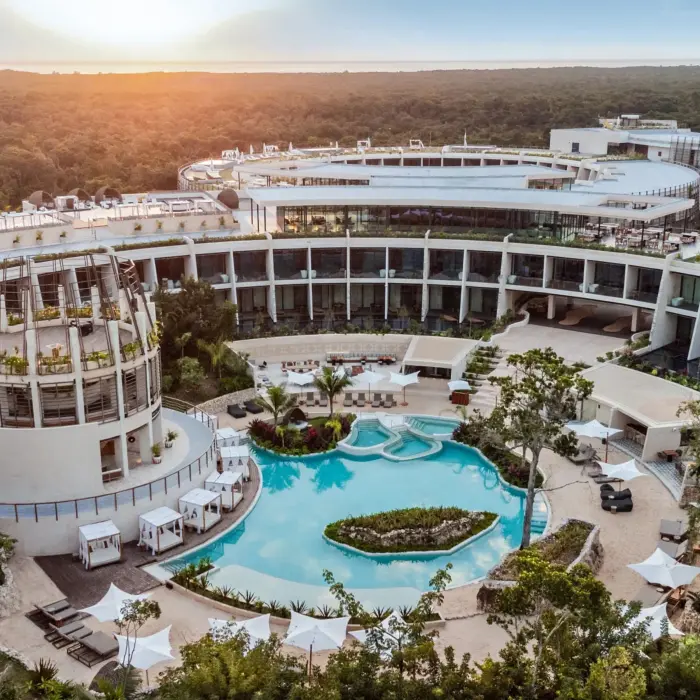 Aerial view of resort architecture with circular buildings, lush greenery, and a lagoon-style pool at sunset.