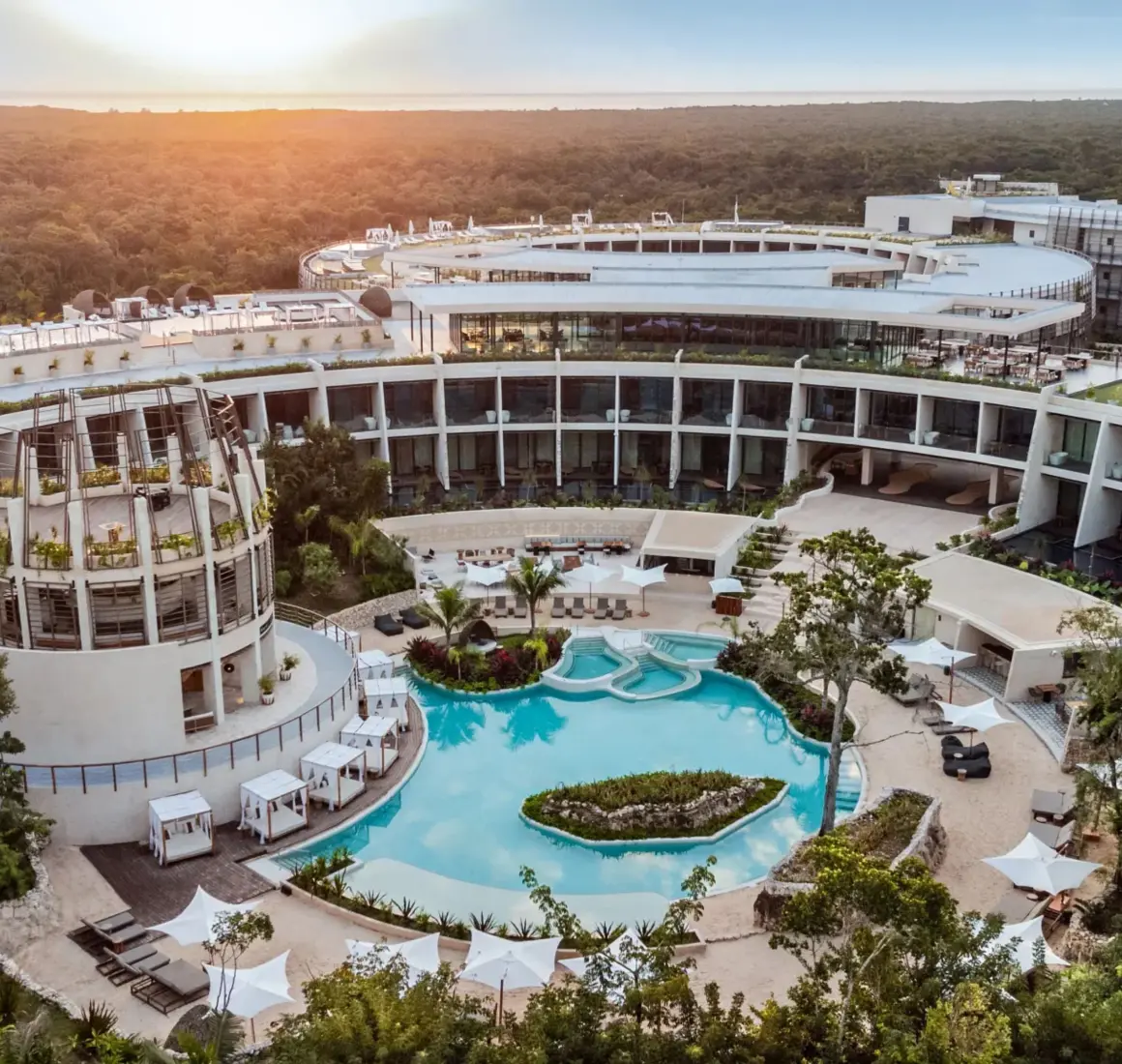Aerial view of resort architecture with circular buildings, lush greenery, and a lagoon-style pool at sunset.