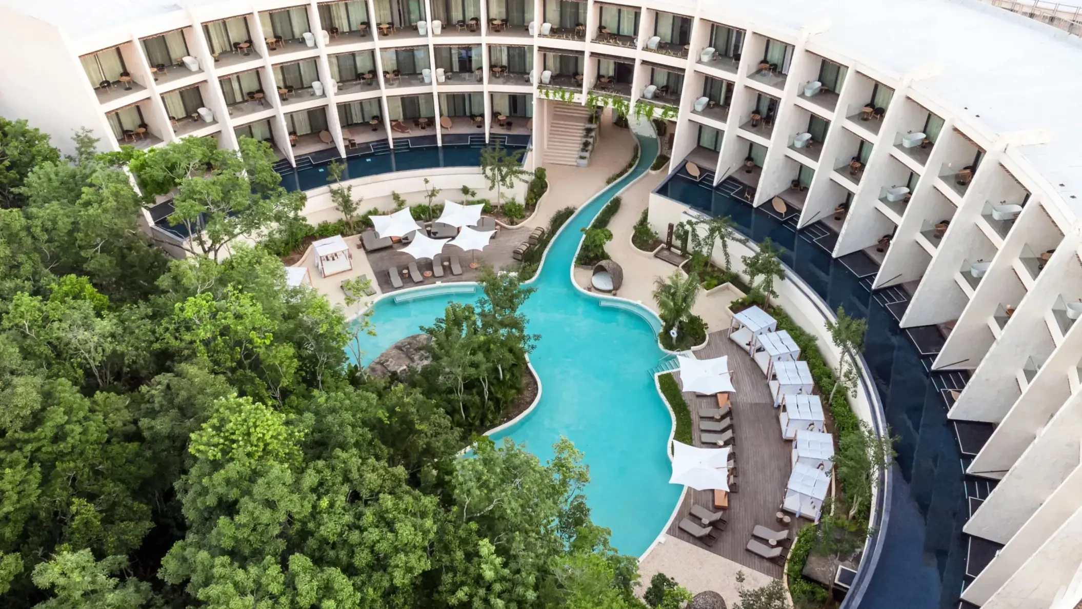 Aerial view of resort with lagoon-style pool, lush greenery, swim-out suites, and private loungers.