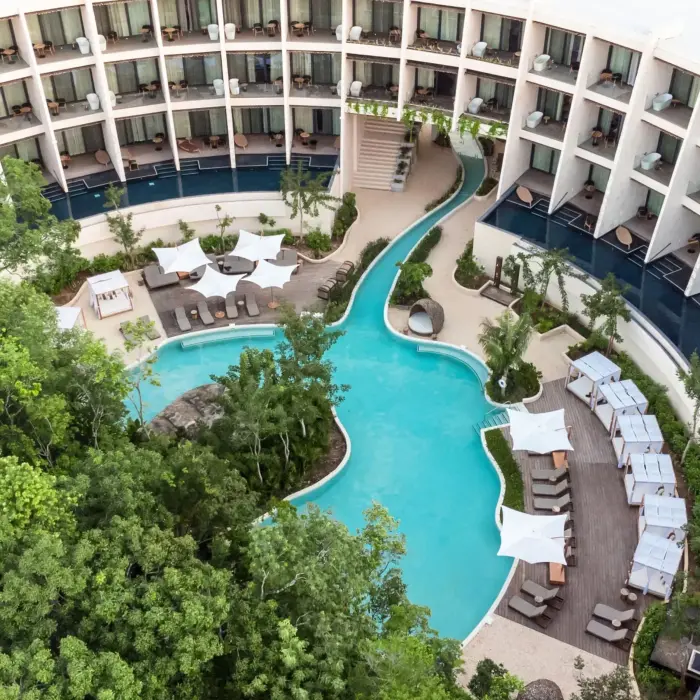 Aerial view of resort with lagoon-style pool, lush greenery, swim-out suites, and private loungers.