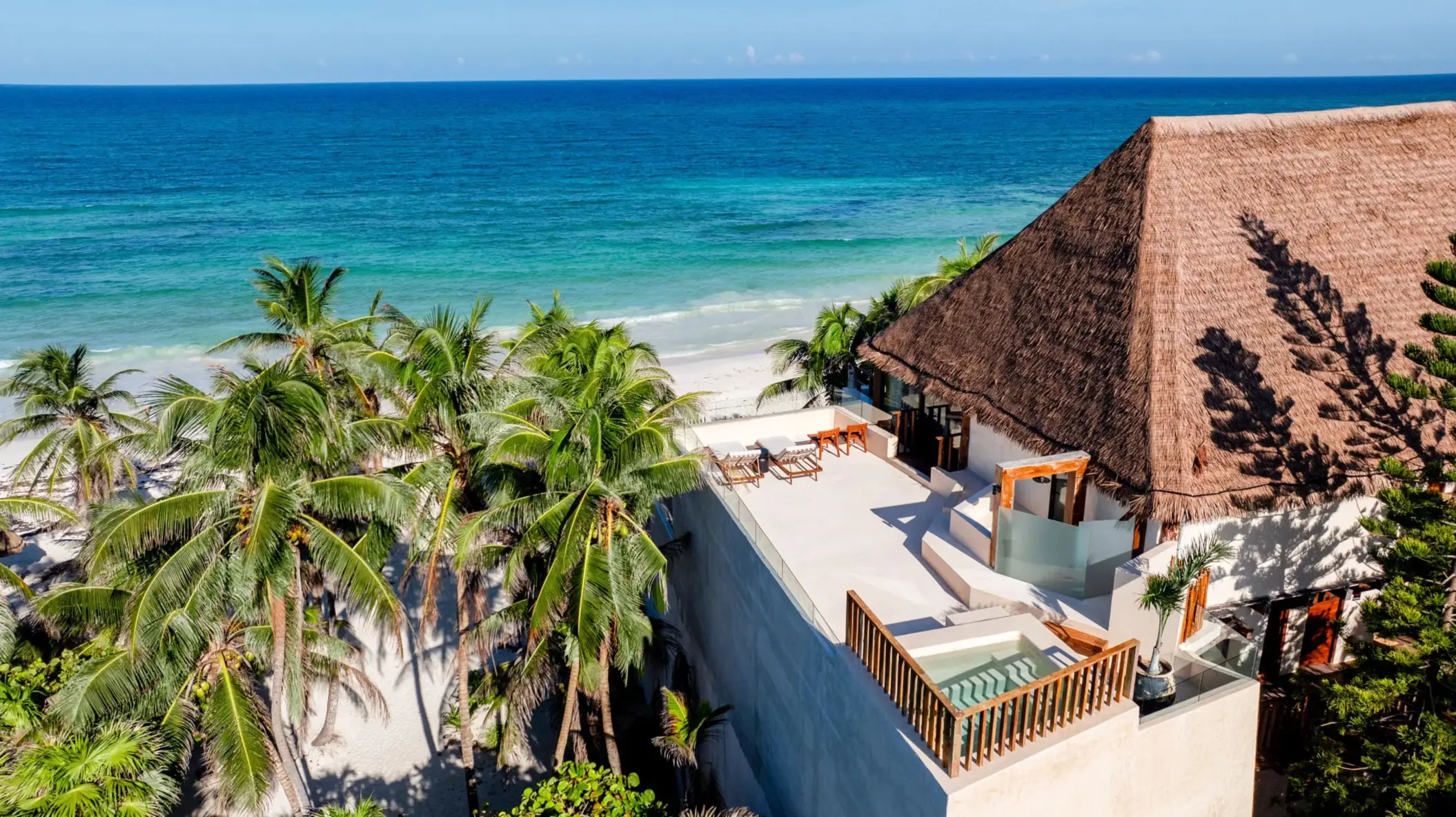 Oceanfront villa with rooftop terrace, thatched roof, and palm trees overlooking turquoise Caribbean waters.