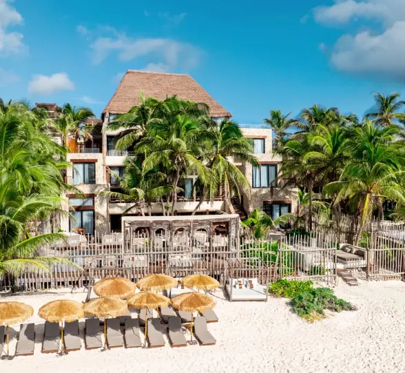 Casa Zamna beachfront with white sand, daybeds under palapas, and tranquil turquoise waters.