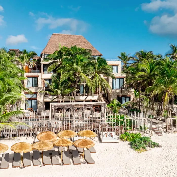 Casa Zamna beachfront with white sand, daybeds under palapas, and tranquil turquoise waters.