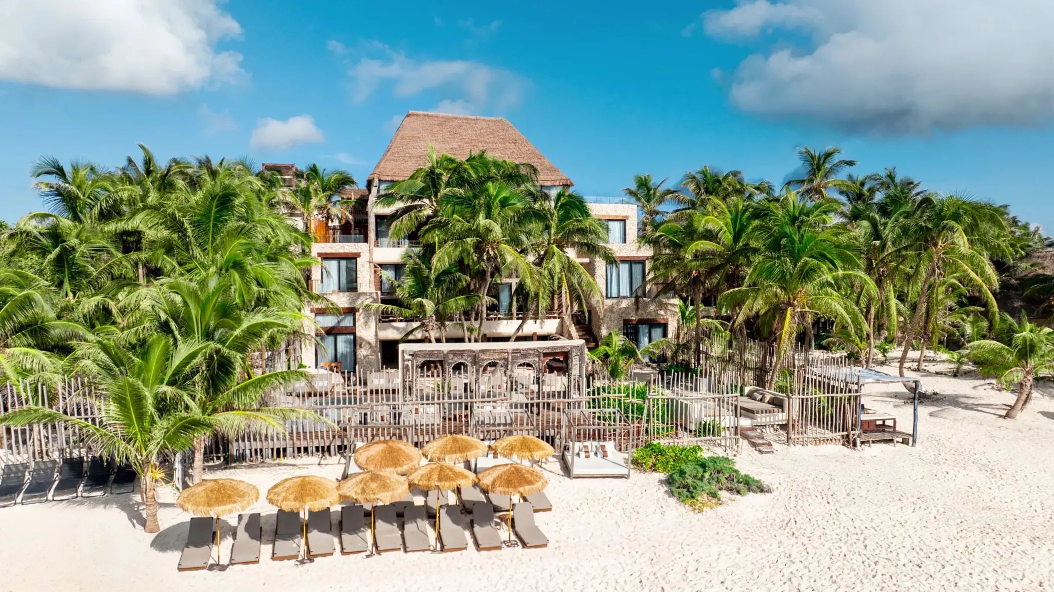 Casa Zamna beachfront with white sand, daybeds under palapas, and tranquil turquoise waters.