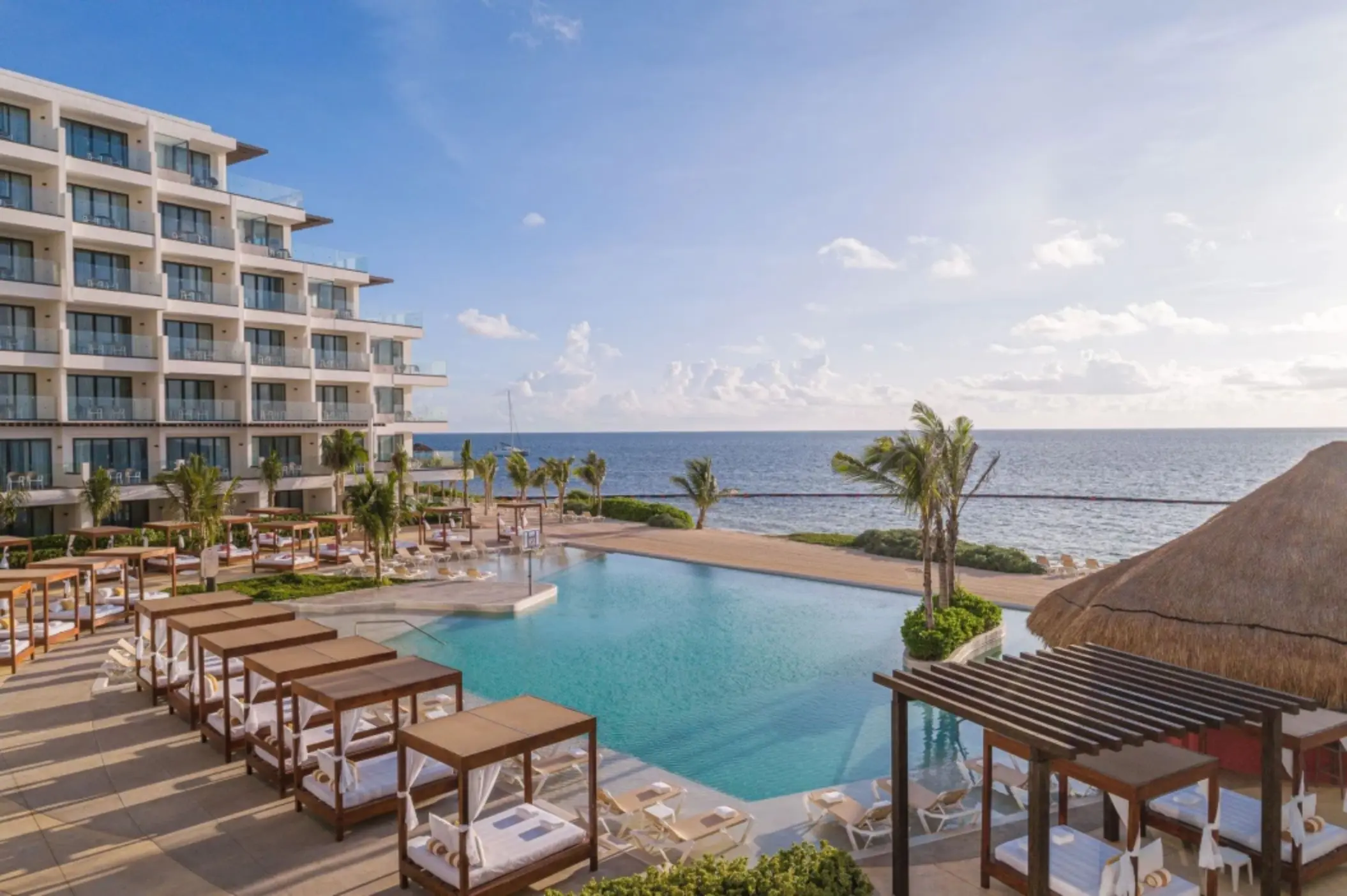 Infinity pool facing the ocean with loungers and canopied daybeds at Sensira Riviera Maya Resort.
