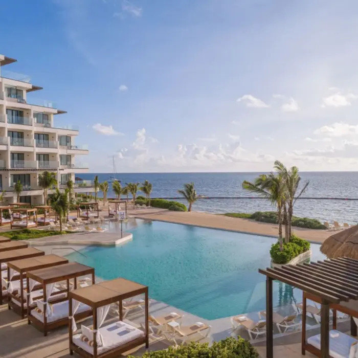 Infinity pool facing the ocean with loungers and canopied daybeds at Sensira Riviera Maya Resort.