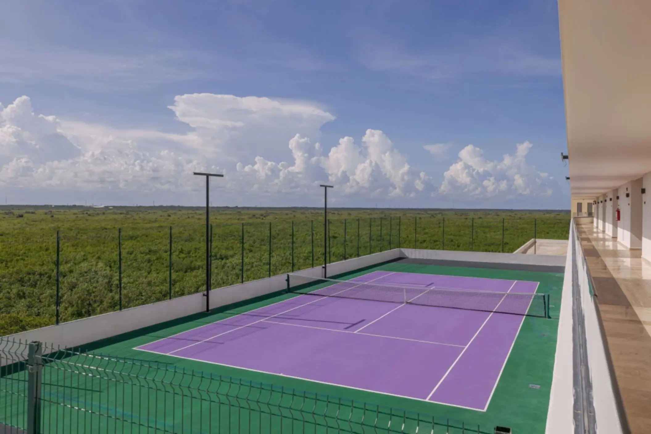 Purple tennis court surrounded by greenery under a bright blue sky at Sensira Resort.