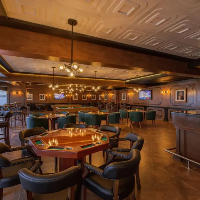 Dimly lit lounge bar with poker tables, green chairs, and vintage-style decor.