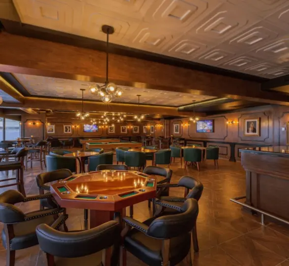 Dimly lit lounge bar with poker tables, green chairs, and vintage-style decor.