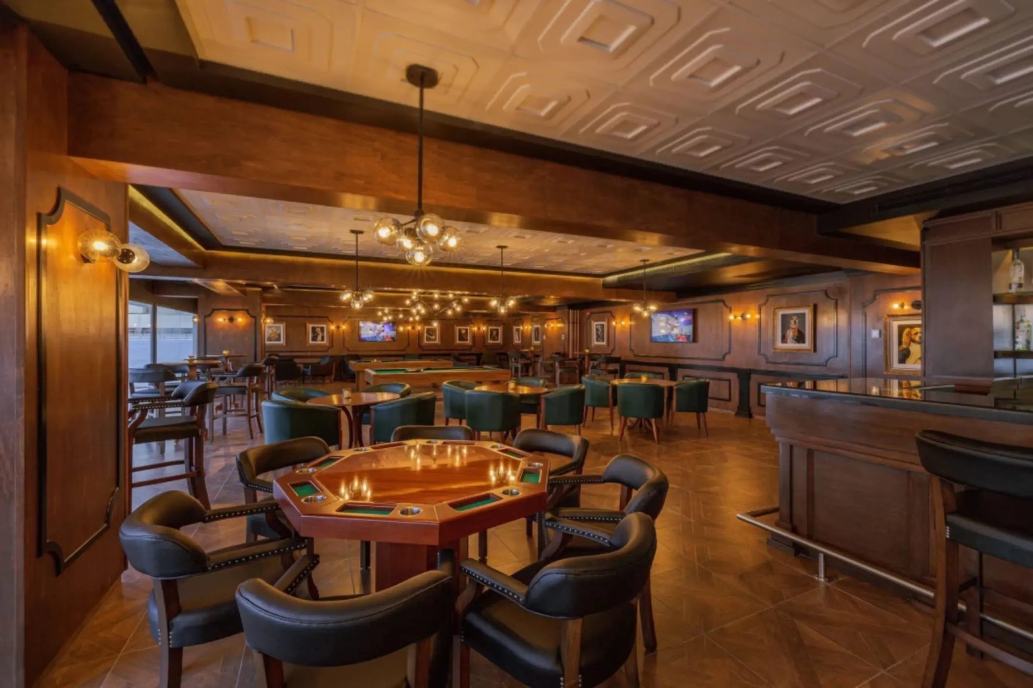 Dimly lit lounge bar with poker tables, green chairs, and vintage-style decor.