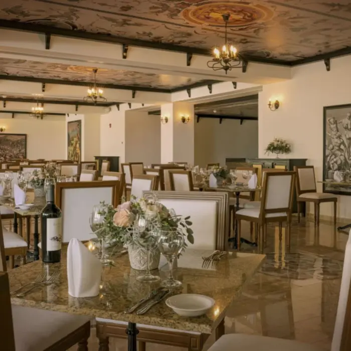 Elegant indoor restaurant with white tablecloths, floral centerpieces, and Renaissance-style artwork.