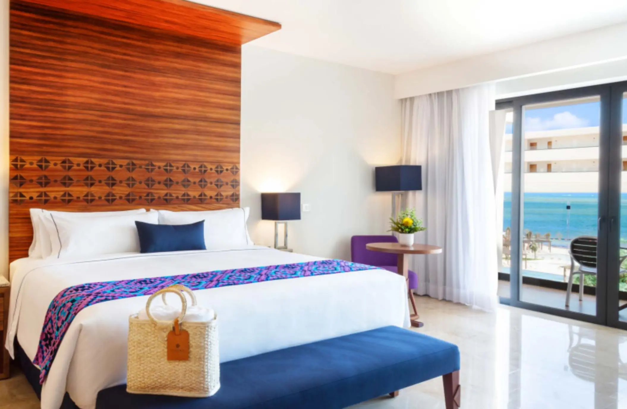 Oceanview room with king bed, blue bench, wood accents, and balcony at Sensira Riviera Maya.