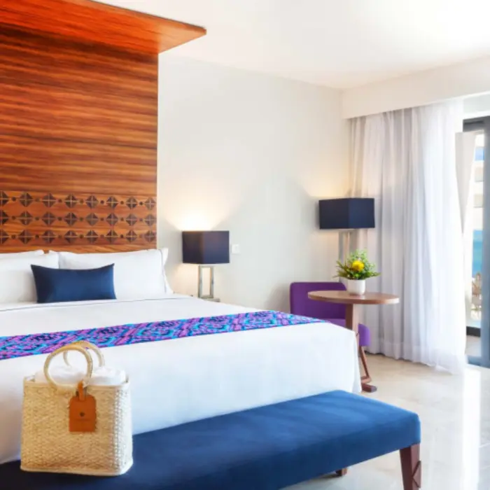 Oceanview room with king bed, blue bench, wood accents, and balcony at Sensira Riviera Maya.