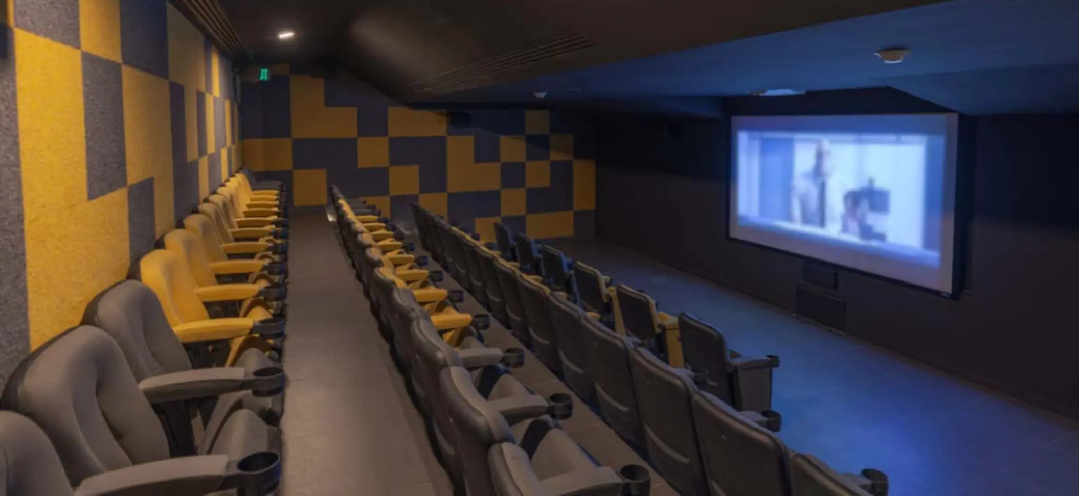 Private cinema with cushioned rows of black and yellow chairs and a large screen showing a movie in dim light.