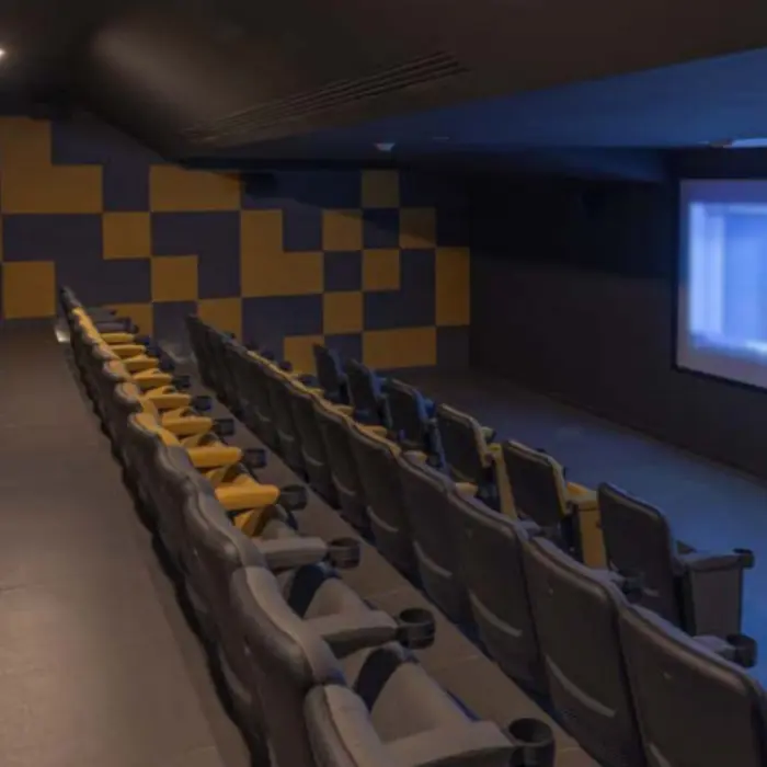 Private cinema with cushioned rows of black and yellow chairs and a large screen showing a movie in dim light.