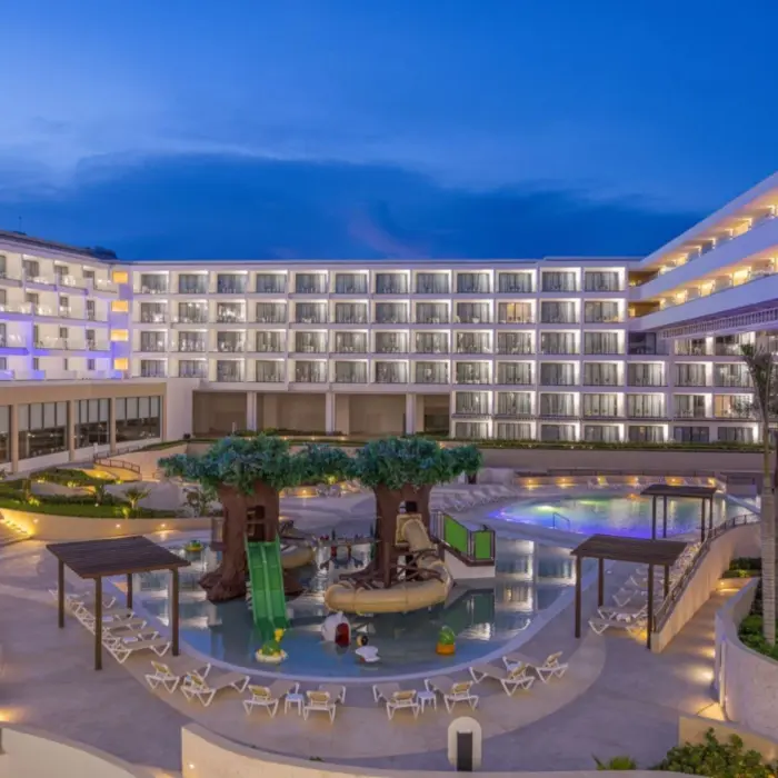 Evening view of kids’ splash zone with tree slides and illuminated hotel balconies surrounding the pool.