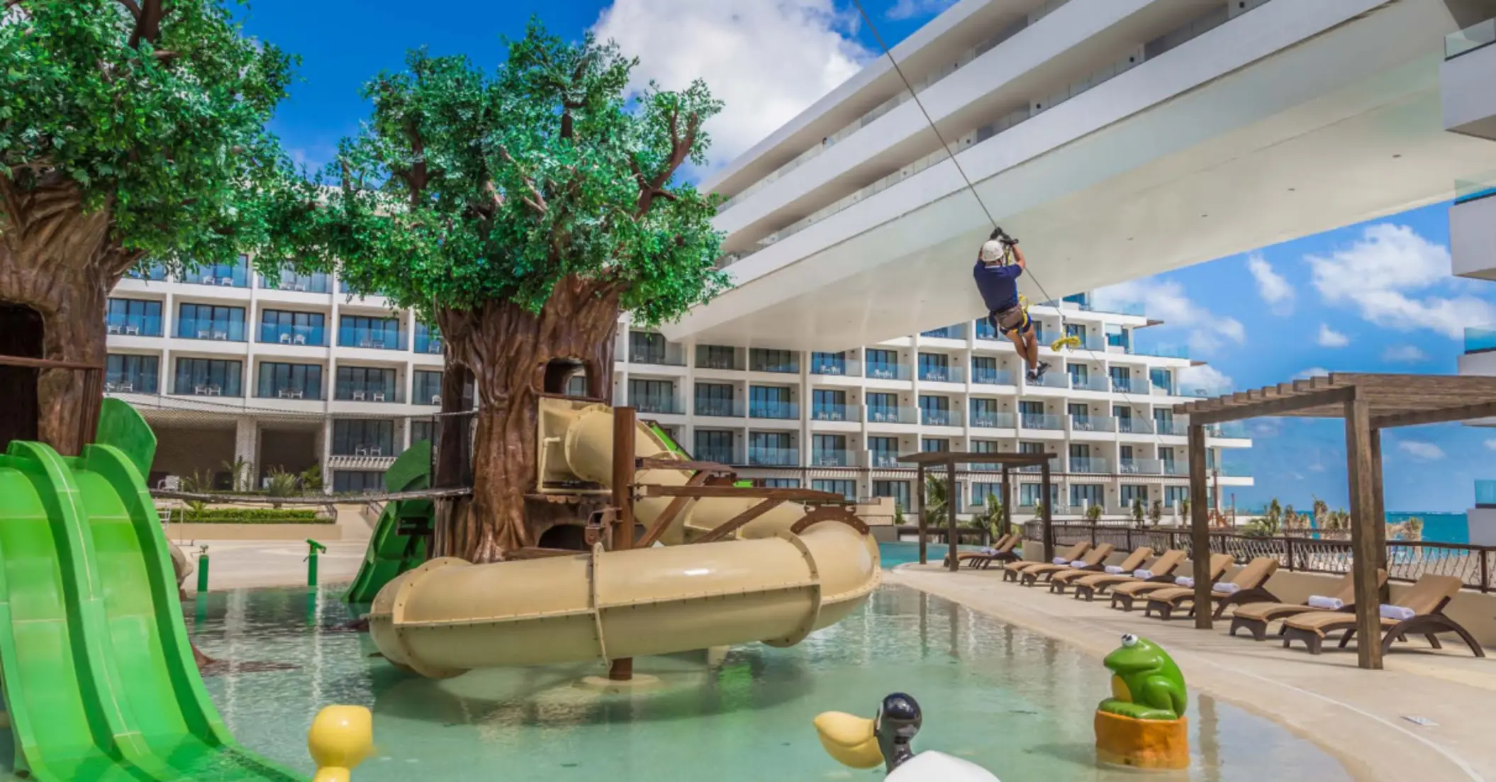 Colorful kids’ water park with treehouse slides and zip line, perfect for family fun by the poolside.