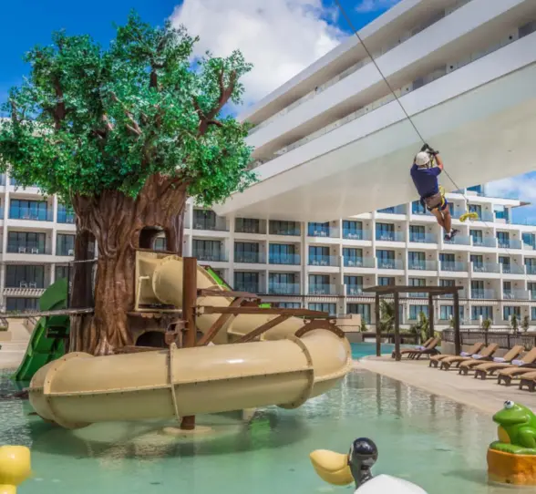 Colorful kids’ water park with treehouse slides and zip line, perfect for family fun by the poolside.