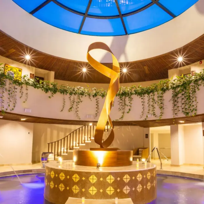 Round spa lobby with cascading vines, a golden sculpture centerpiece, and soft glowing lights.