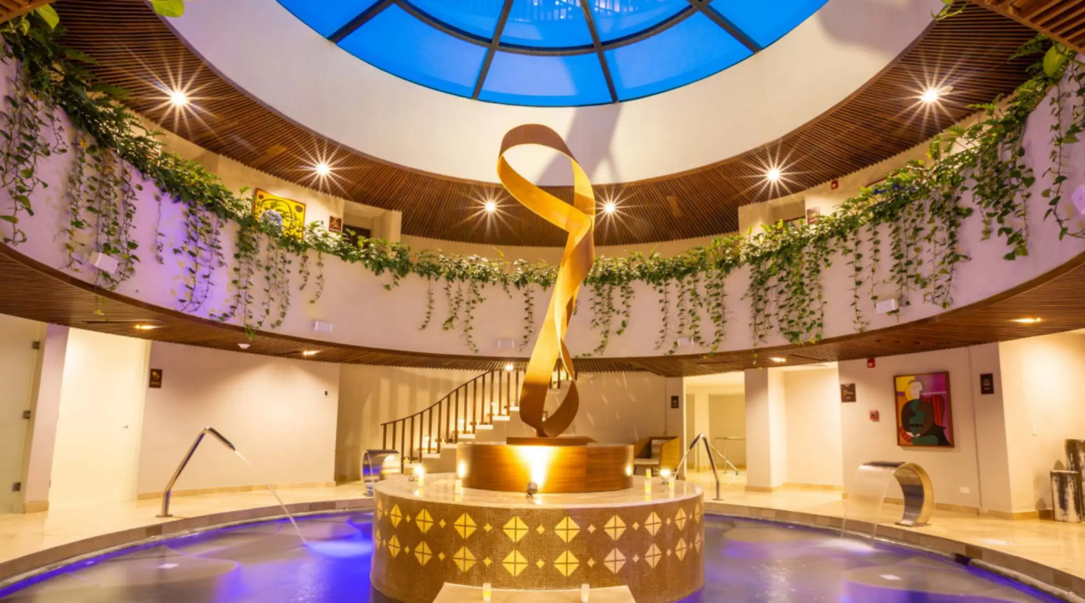 Round spa lobby with cascading vines, a golden sculpture centerpiece, and soft glowing lights.
